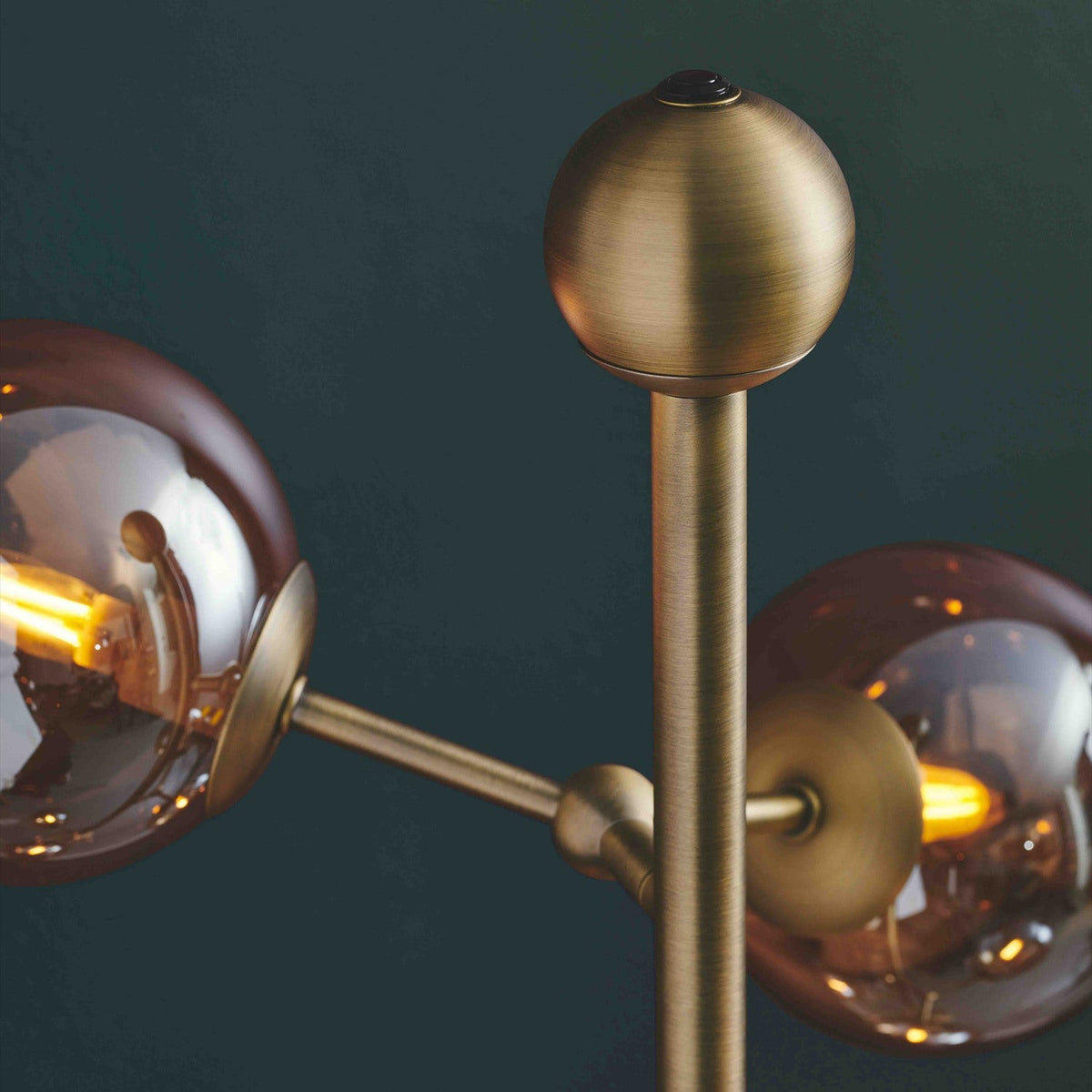 Close-up of the Atom 6 Light Floor Lamp in antique brass, showing a round finial and amber glass spheres branching from the vertical rod against a dark background.