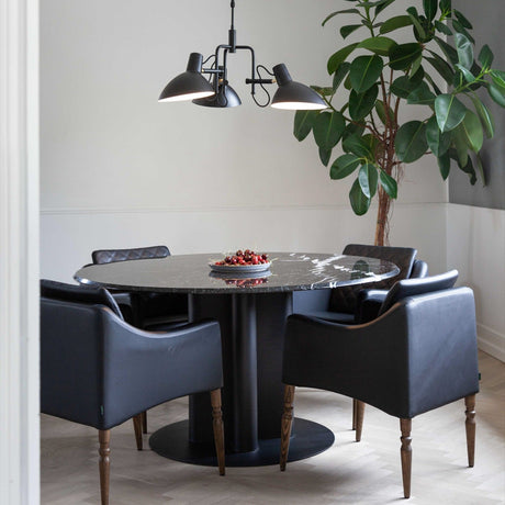 Metropole 3 Light Flush Ceiling Light in black, with dome-shaped shades on short arms and a central cone, hung above a round marble dining table in a living space.