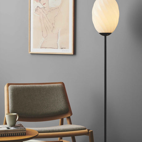 Twist Oval Floor Lamp in opal and black, twisted-flute glass shade on a slim black stem, shown beside an armchair and framed art in a living room.