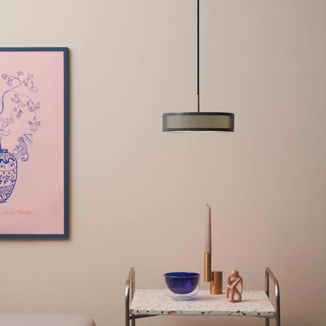 Frame 3 Light Pendant Light 24cm in black and antique brass, a drum shade with perforated mesh sides, hung above a side table in a living room setting.