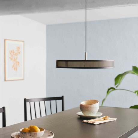Frame 5 Light Pendant Light 43cm in black and antique brass, a wide drum shade with perforated mesh band, hung above a dining table in a light blue-walled room.