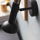 Torch Wall Pendant Light in black and antique brass, close-up of the angled tube, brass collar, knuckle joint, and round wall plate against a softly blurred interior.