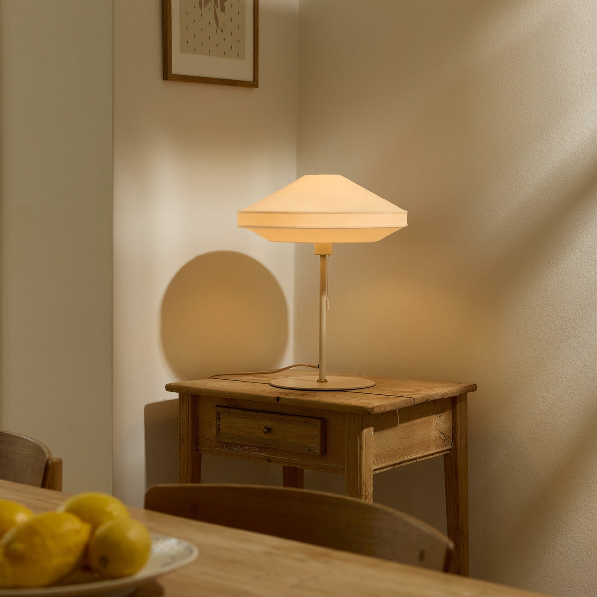 Paris Silk Table Lamp in natural cream fabric with a two-tier shade on a slim stem and round base, shown lit on a wooden side table.