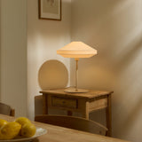 Paris Silk Table Lamp in natural cream fabric with a two-tier shade on a slim stem and round base, shown lit on a wooden side table.