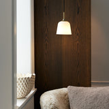 Room Pendant Light 15cm in opal glass with antique brass collar, shown lit above a window sill in a living room with wood panelling and a cream armchair.