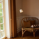 Room Floor Lamp in opal glass and antique brass, tall slim curved stem with round base, shown beside a rattan sofa with cushions in a living room corner.