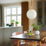 Stockholm Pendant Light 30cm in marble brown, a spherical opal glass shade with amber marbling hung from a brass ring, shown above a wooden dining table in a kitchen setting.