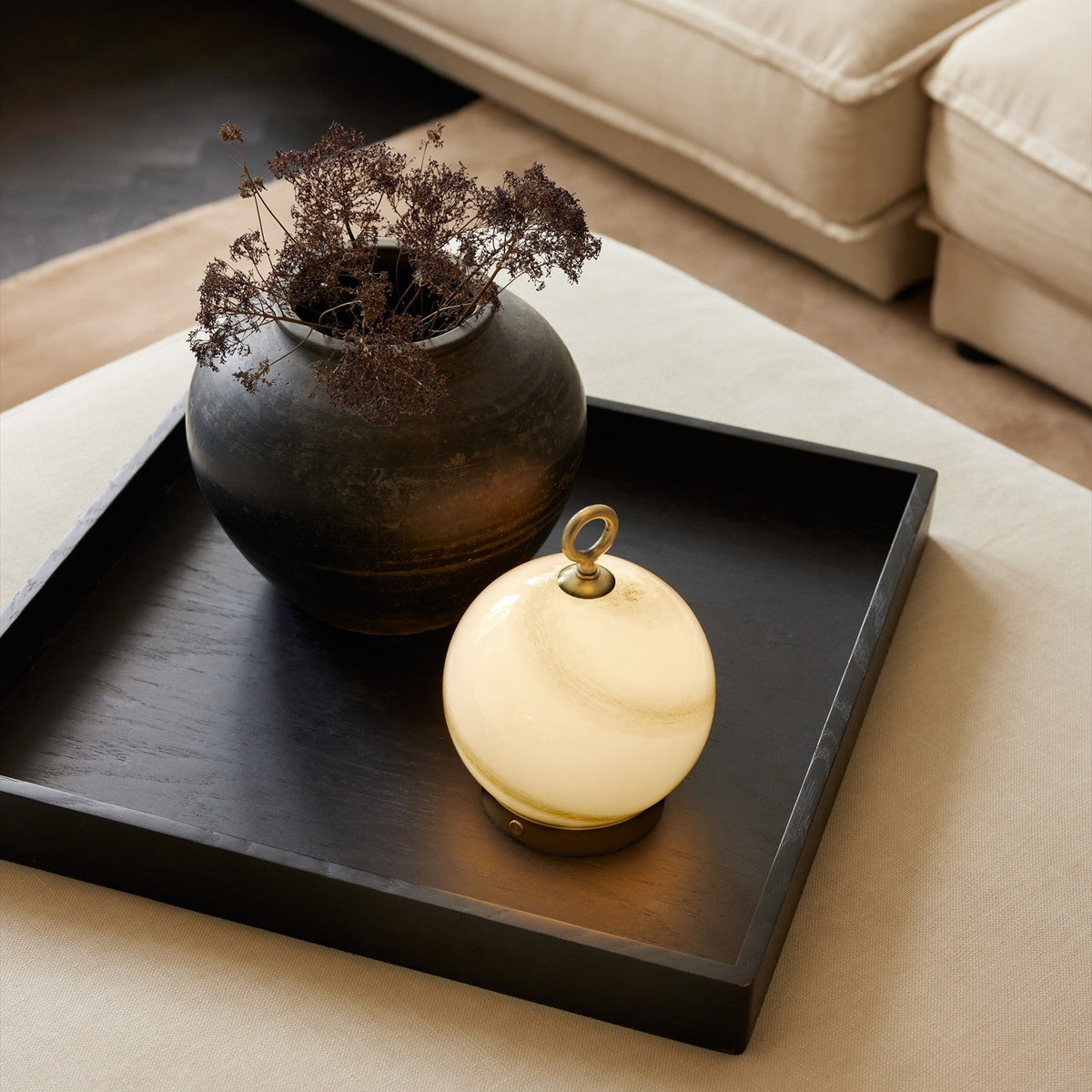 Stockholm LED Rechargeable Outdoor Table Lamp in marble grey with a brass base and ring top, glowing beside a dark ceramic vase on a black tray table.