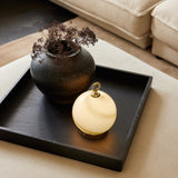 Stockholm LED Rechargeable Outdoor Table Lamp in marble grey with a brass base and ring top, glowing beside a dark ceramic vase on a black tray table.