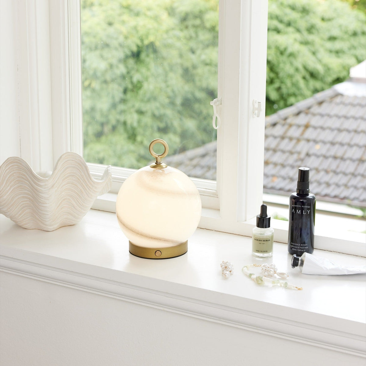 Stockholm LED Rechargeable Outdoor Table Lamp in marble grey, spherical opal glass shade with brass ring handle and base, shown on a white windowsill beside decor items.