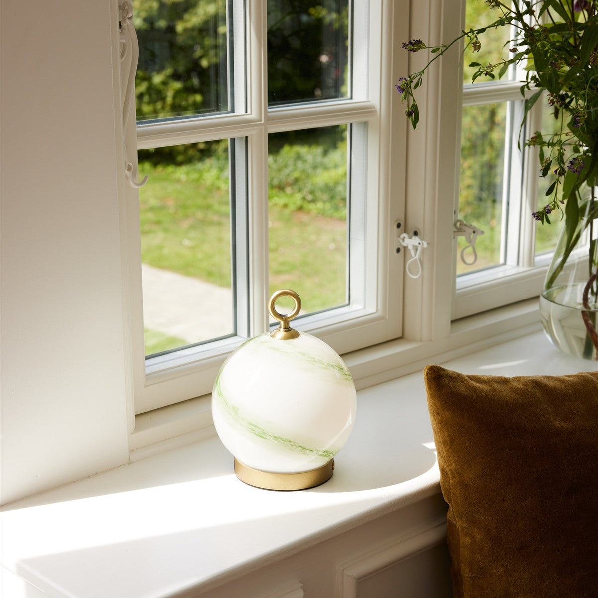 Stockholm LED Rechargeable Outdoor Table Lamp 15cm in Marble Green, an opal glass globe with green marbled streaks on a brass base and ring handle, shown on a windowsill.