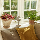 On the Move LED Rechargeable Table Lamp in white with round drum shade on slim stem, shown on a windowsill beside potted plants and cushions.