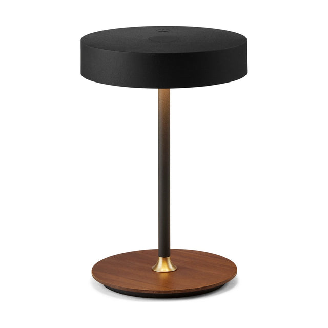 On the Move rechargeable LED table lamp with a black drum shade on a slim black stem, brass collar, and round walnut wood base, on a plain white background.