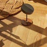 On the Move LED rechargeable table lamp, 13cm, gunmetal drum shade on slim stem with walnut disc base and brass collar, shown on a wooden floor.
