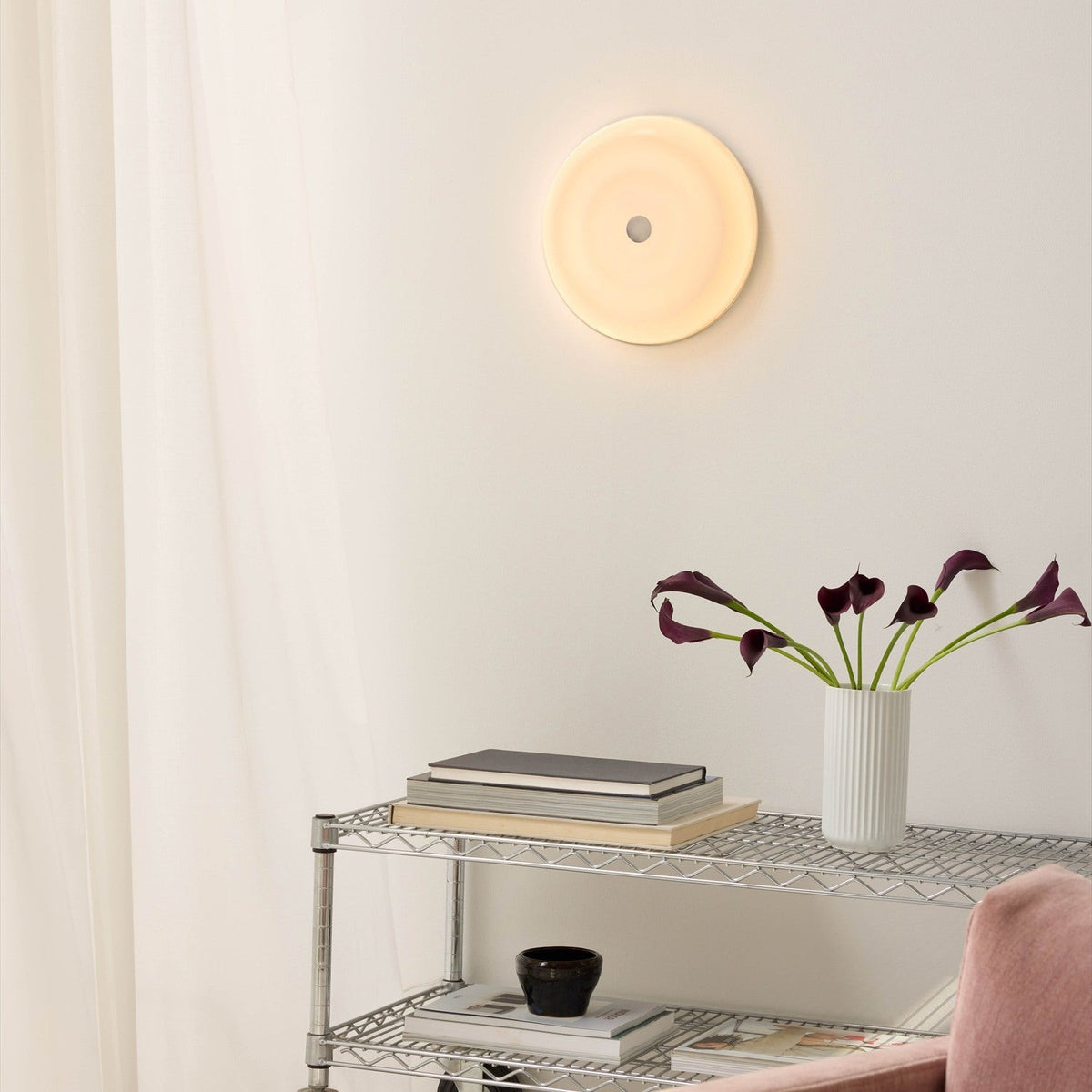 Wave LED Dimmable 3-Step Flush Ceiling Light in opal glass with concentric ring detail, mounted on a wall above a shelving unit with books and a vase of flowers.