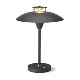 Stepp LED Outdoor Table Lamp in black, with a wide flat disc shade, brass cap and cone detail on top, slim stem, and round base, shown on a plain white background.