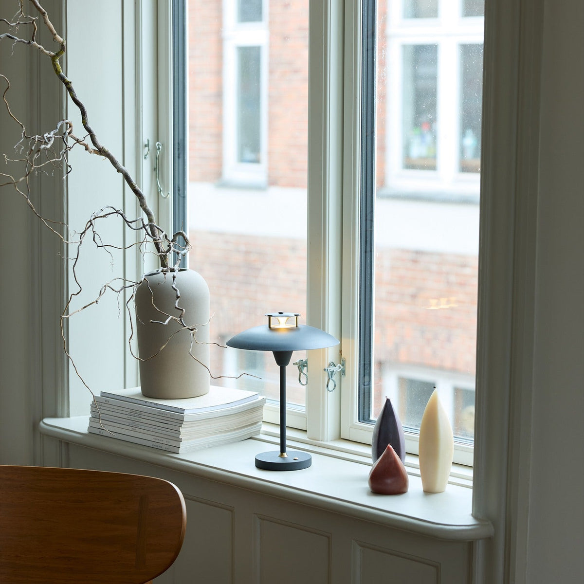 Stepp LED Outdoor Table Lamp in black on a windowsill, with a wide flat disc shade and slim stem, shown lit beside a ceramic vase and decorative ornaments.