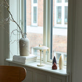 Stepp LED Outdoor Table Lamp in cream on a windowsill, with a shallow disc shade, slim stem, and round base beside a vase, candles, and stacked books.