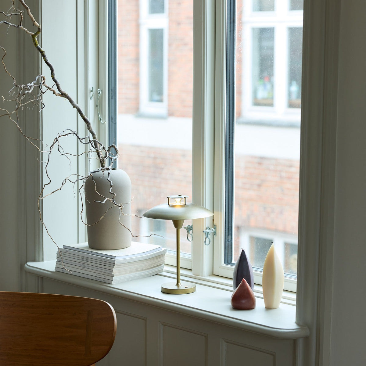 Stepp LED Outdoor Table Lamp in antique brass with a shallow disc shade on a slim stem, shown lit on a window sill beside vases and candle ornaments.