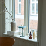 Stepp LED Outdoor Table Lamp in dark green with a wide flat disc shade and slim stem, shown on a window ledge beside a ceramic vase and candles.