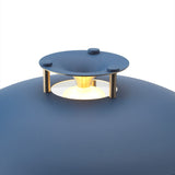 Close-up of the Stepp LED Outdoor Table Lamp in dark blue, showing the flat disc cap on brass posts glowing above the rounded blue base, set against a plain white background.