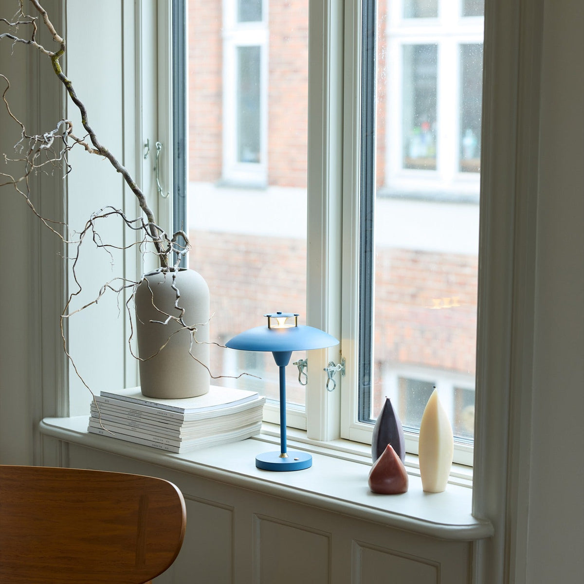 Stepp LED Outdoor Table Lamp in dark blue with a shallow disc shade and slim stem, shown on a window sill beside candles and a ceramic vase.
