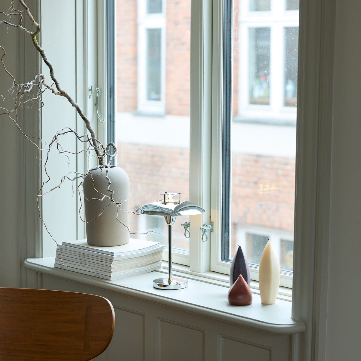 Stepp LED Outdoor Table Lamp in chrome with a flat flared disc shade and round base, shown lit on a windowsill beside a ceramic vase and decorative ornaments.