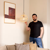 Stockholm Nordic Edition Pendant Light 30cm in natural bamboo with brass collar, shown lit in a living room beside a man for scale reference.