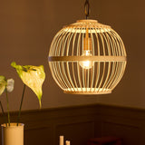 Stockholm Nordic Edition Pendant Light 40cm in natural bamboo, a round woven cage with a visible bulb, hung above a dining table in a warm-toned room.