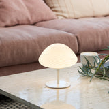 Mini Mush Glass Cable Table Lamp in white, with a ribbed opal glass dome shade on a slim stem and round disc base, shown lit on a marble coffee table beside a sofa.