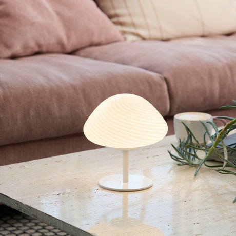 Mini Mush Glass Cable Table Lamp in white, with a ribbed opal glass dome shade on a slim stem and round disc base, shown lit on a marble coffee table beside a sofa.