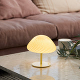 Mini Mush Glass Cable Table Lamp in cream, its ribbed dome shade glowing on a slim black stem, shown lit on a coffee table beside a sofa.