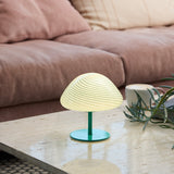 Mini Mush Glass Cable Table Lamp in turquoise with a wide spiral-fluted mushroom dome on a slender green stem and round base, shown lit on a coffee table beside a sofa.