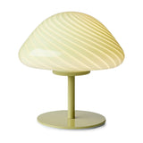 Olive green Mini Mush glass table lamp with a low mushroom-shaped dome shade featuring a spiral flute design in warm butter cream tones, on a slender metal stem and round base.