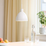 Rock Pendant Light 20cm in white, dome-shaped shade with matt finish, hanging above a dining table with glasses, a bottle, and a fruit bowl in a bright room.
