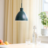 Rock Pendant Light 20cm in green, dome-shaped metal shade with white interior, hanging above a dining table set with glassware and a water bottle near sheer curtains.