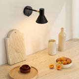 Style wall light in black and antique brass with a downward-facing cone shade, mounted above a kitchen counter styled with ceramic vases and fruit.
