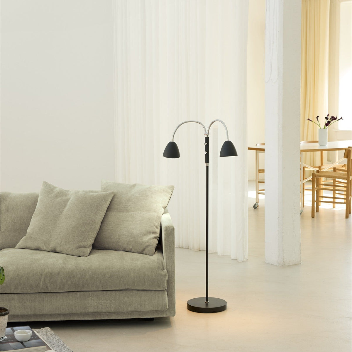 Room 2-light floor lamp in black and chrome, slim stem on a round disc base with two adjustable chrome goosenecks and black cone shades, shown in a living room setting.