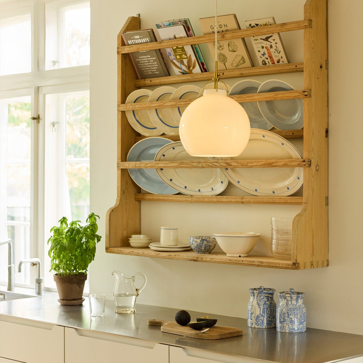 Toscana Pendant Light 36cm in opal glass with a brass cradle and cable, shown lit above a wooden plate rack in a kitchen setting.