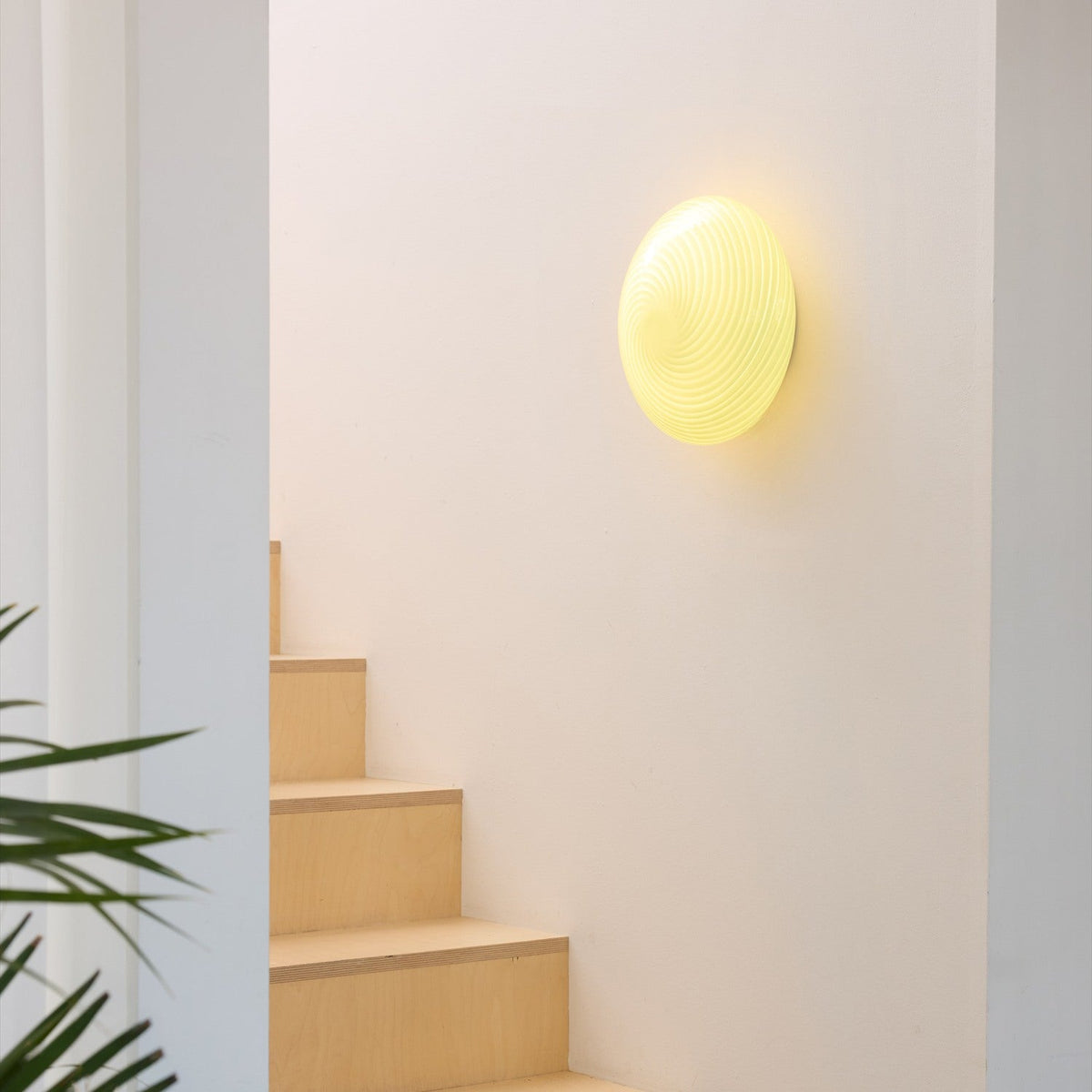 Candy Flush Ceiling Light 30cm in cream, a round wall-mounted opal glass dome with a spiral ribbed texture, glowing warmly beside a wooden staircase.