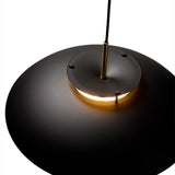 Close-up of the Stepp LED Pendant Light in black and antique brass, showing the shallow disc shade, brass centre fitting, and warm downward glow against a white background.
