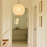 Balloon Pendant Light 40cm in white and beige, a pleated fabric globe with brass top and bottom rings, hung in a hallway leading to a bathroom with framed art nearby.