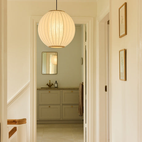 Balloon Pendant Light 40cm in white and beige, a pleated fabric globe with brass top and bottom rings, hung in a hallway leading to a bathroom with framed art nearby.