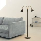 Space LED 2F Floor Lamp in black and antique brass, with two curved goosenecks and cone shades on a slim stem, shown beside a grey sofa.