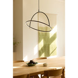Tilt LED Ring Chandelier 60cm in black and brass, with a lit horizontal ring crossed by a black arched loop, hanging above a wooden dining table in a sunlit room.