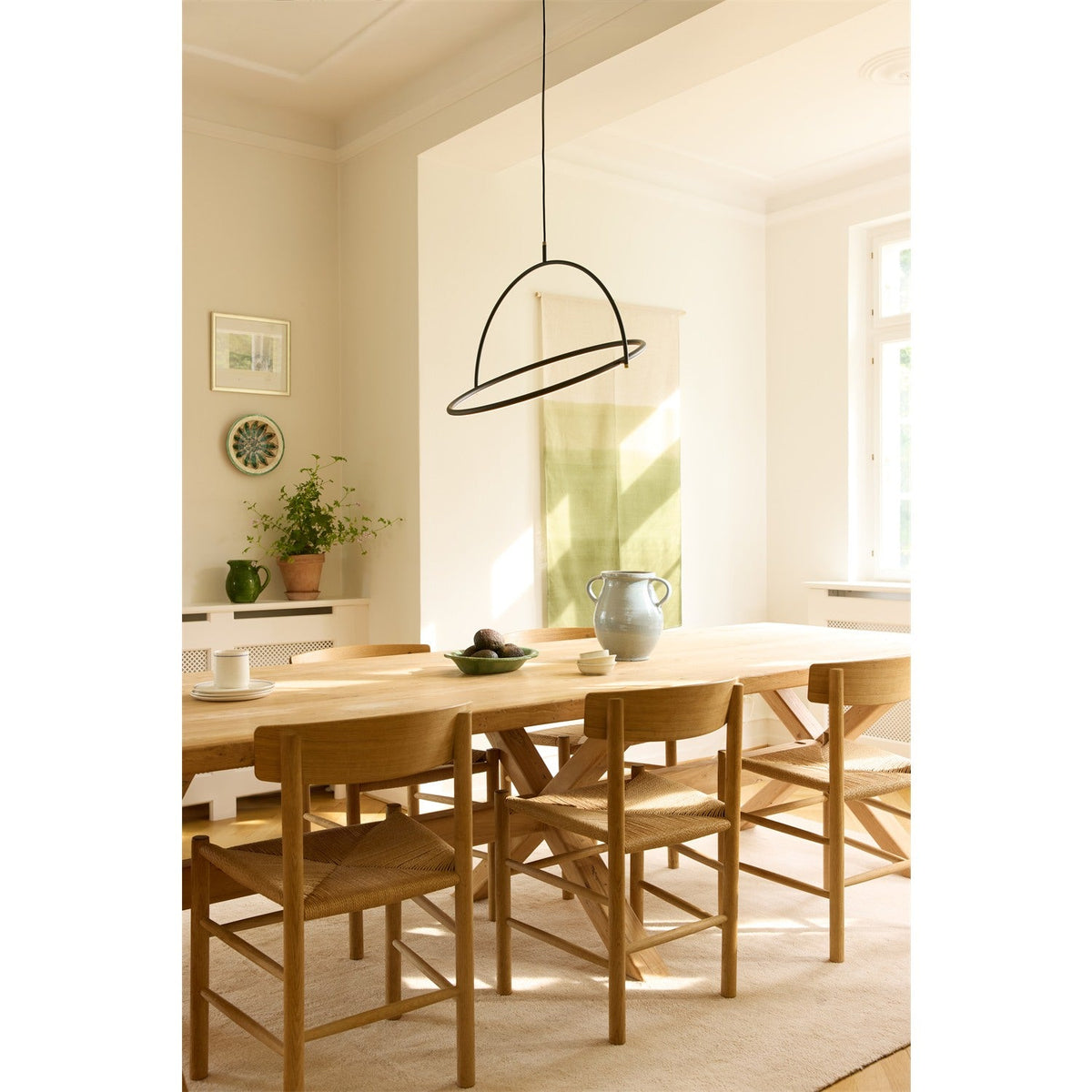 Tilt LED Ring Chandelier 40cm in black and brass hangs above a wooden dining table, its horizontal ring and crossing arch suspended from a single black flex in a bright, neutral-toned dining room.