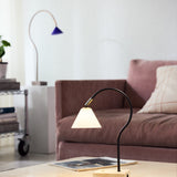 Question LED Glass Portable Table Lamp with black curved rod, conical opal glass shade, antique brass fitting, and travertine base, shown lit on a coffee table in a living room.