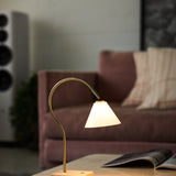 Question LED portable table lamp with a conical opal glass shade on a curved antique brass rod and travertine base, lit on a table beside a sofa in a living room.