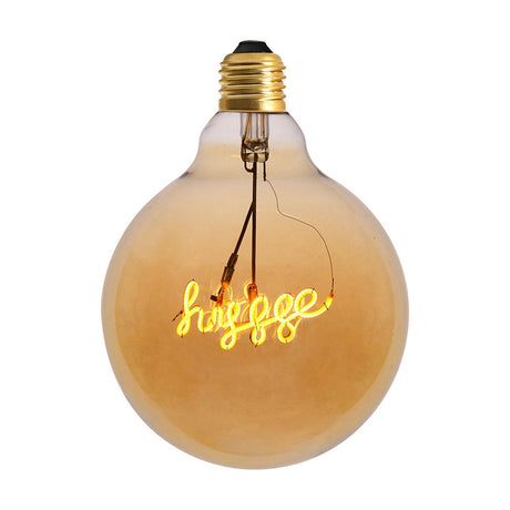 Colors Hygge LED G125 E27 2.5W Bulb, a large round amber glass bulb with brass-coloured screw fitting and a cursive "hygge" filament glowing across the centre, shown on a plain white background.