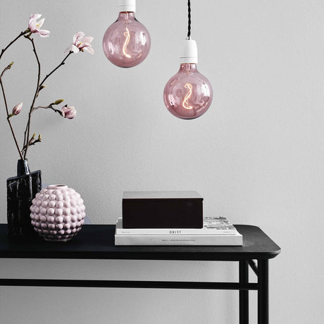 Two Colors Soft LED G125 3-Step Bulbs in rose glass with visible S-shaped filaments, hanging on pendant cords above a black console table.